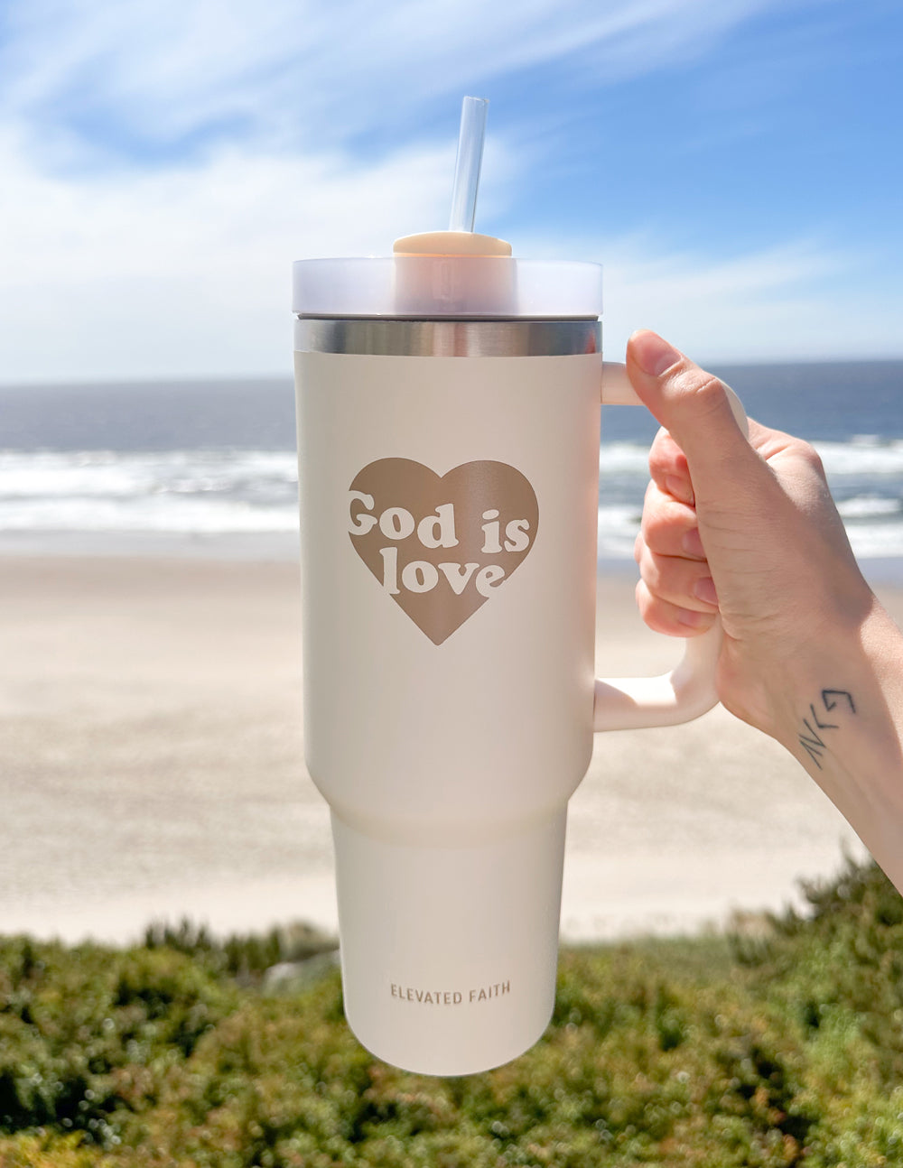 40 oz tumbler with straw, cream body, silver lid band, hand holding handle, heart print