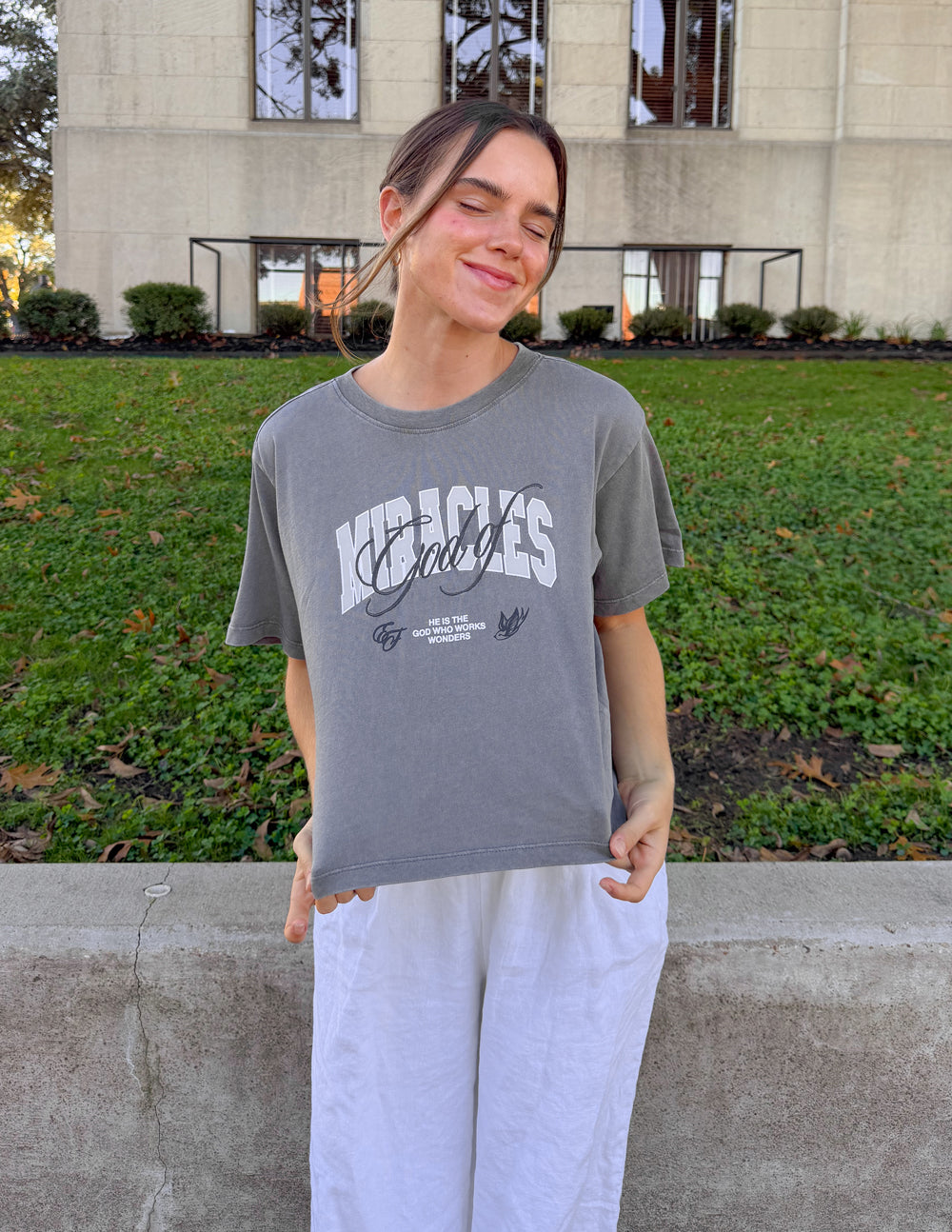 Cropped gray women’s tee with “Miracles” graphic centered on the chest
