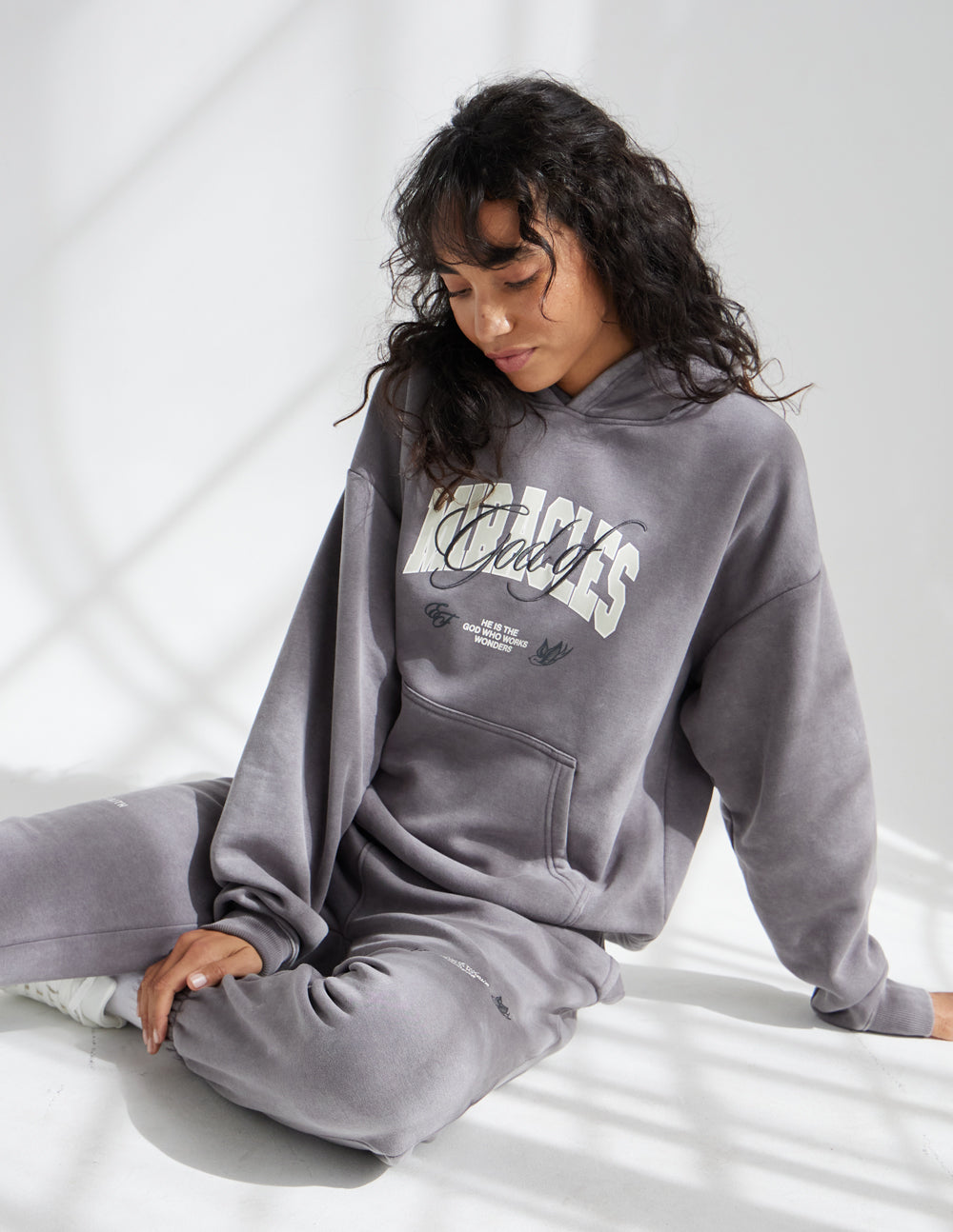 Grey unisex hoodie with hood and kangaroo pocket, worn while seated