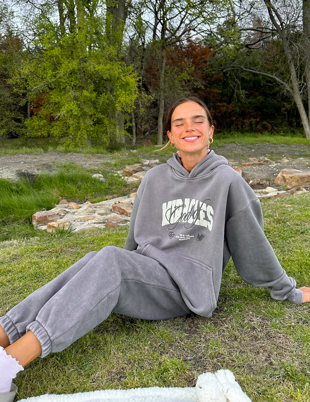 Grey unisex hoodie with front script logo and kangaroo pocket, relaxed seated