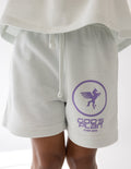 White kids racing shorts with purple logo emblem on leg