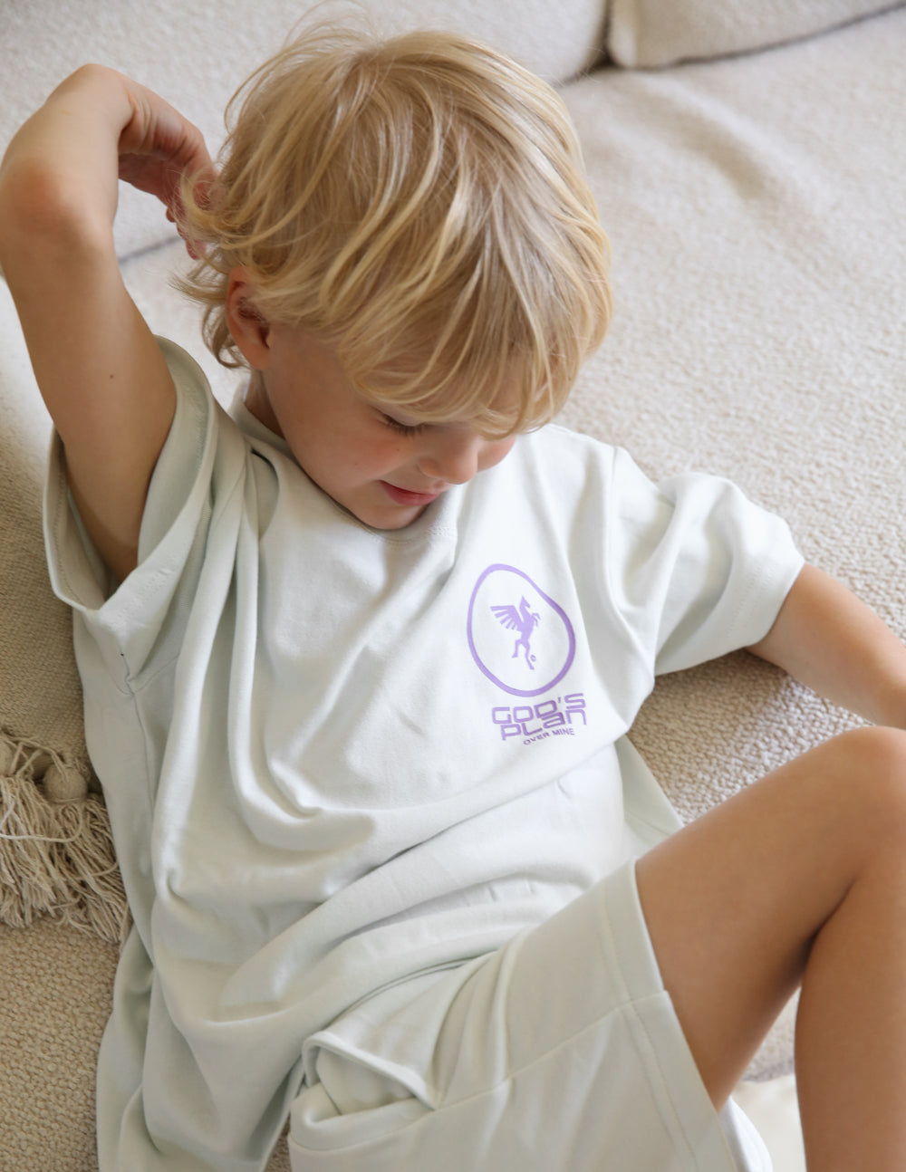 Kids racing T-shirt in white with purple chest logo on a child by the sofa