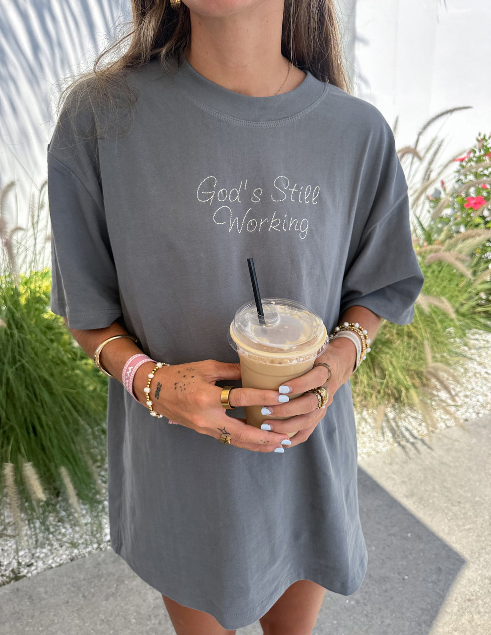 Unisex heather-gray graphic tee with cursive 'God's Still Working' front text