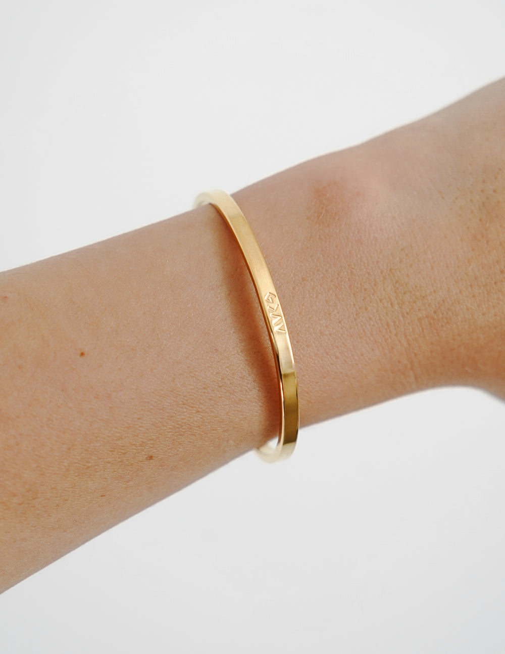 Gold cuff bracelet side view with engraved lettering on the band
