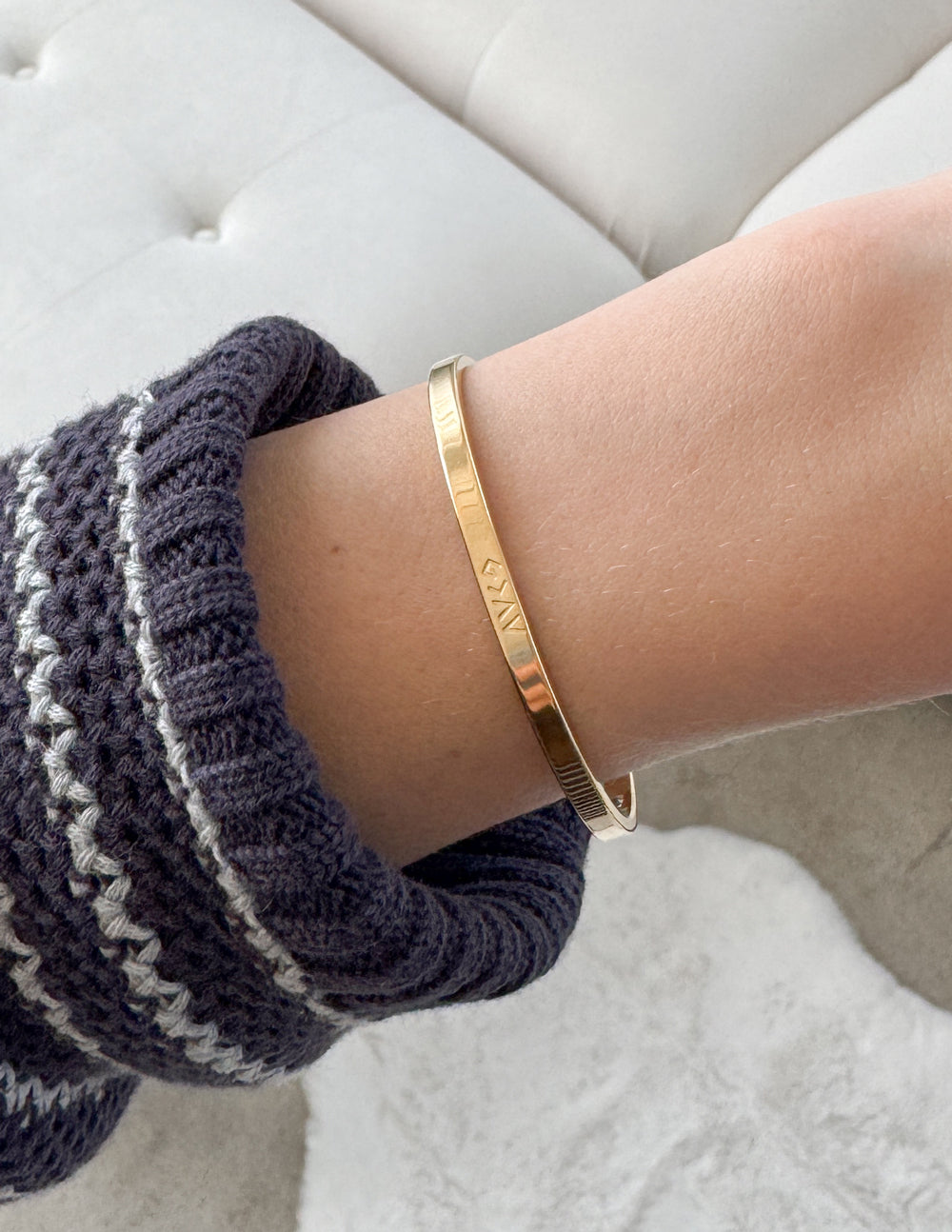 Gold cuff bracelet with engraved lettering on wrist over knit cuff