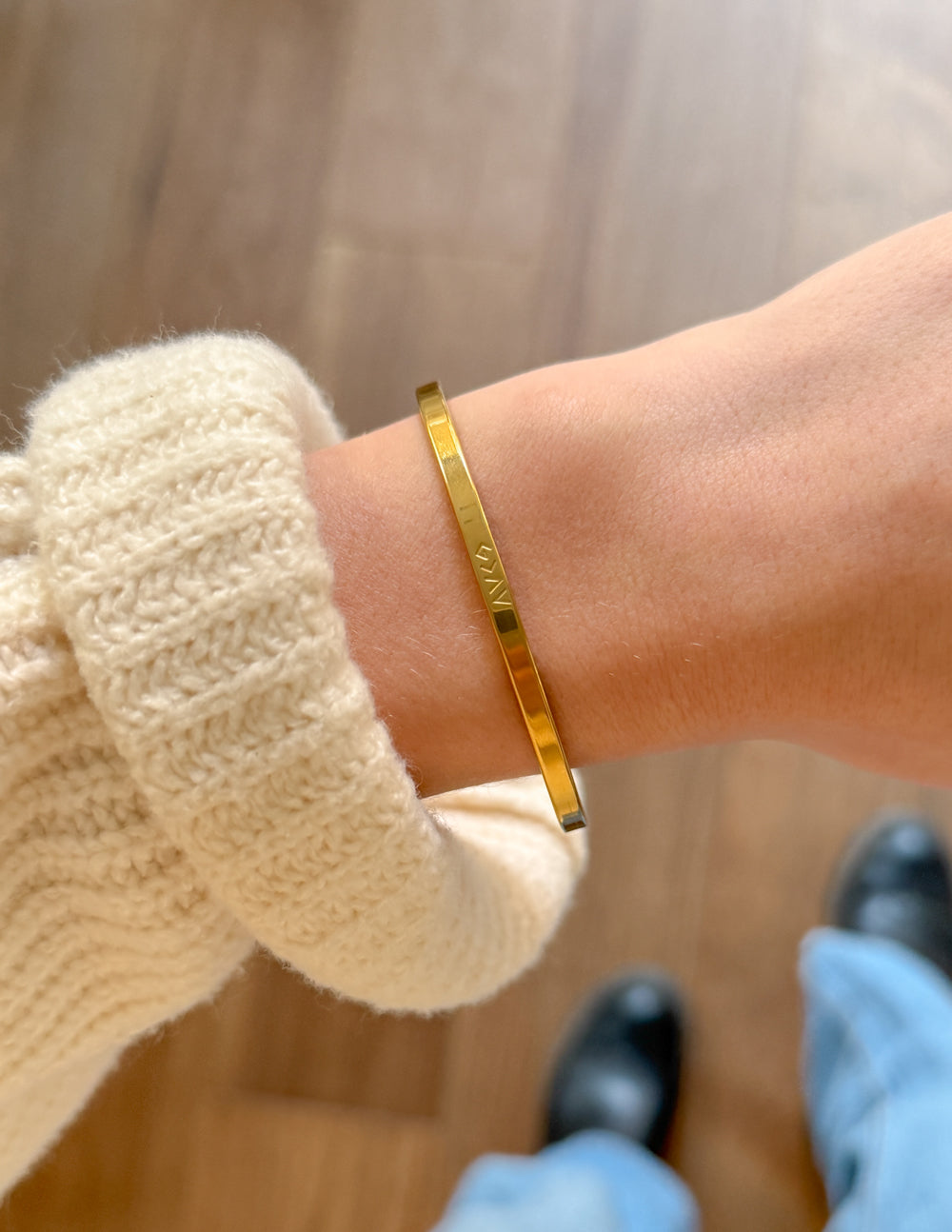 Gold cuff bracelet with engraved lettering on wrist over knit sweater cuff