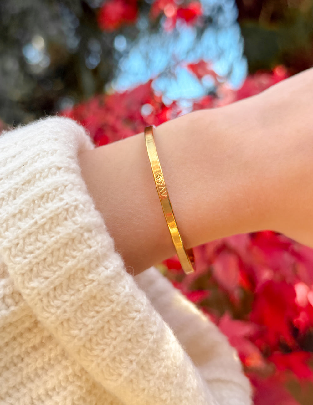 Gold cuff bracelet on wrist, engraved lettering across the band