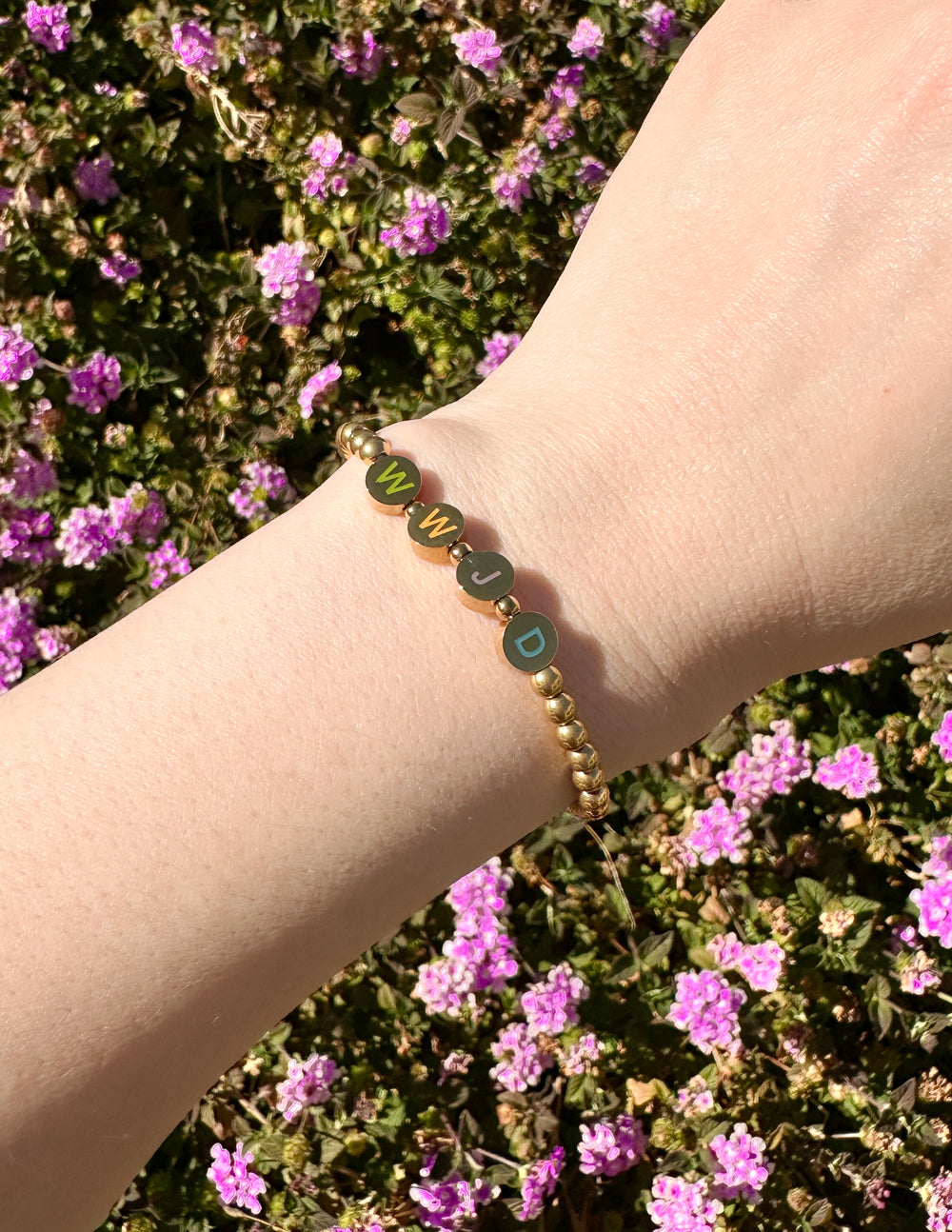 Gold beaded bracelet with dark and light letter charms on the wrist