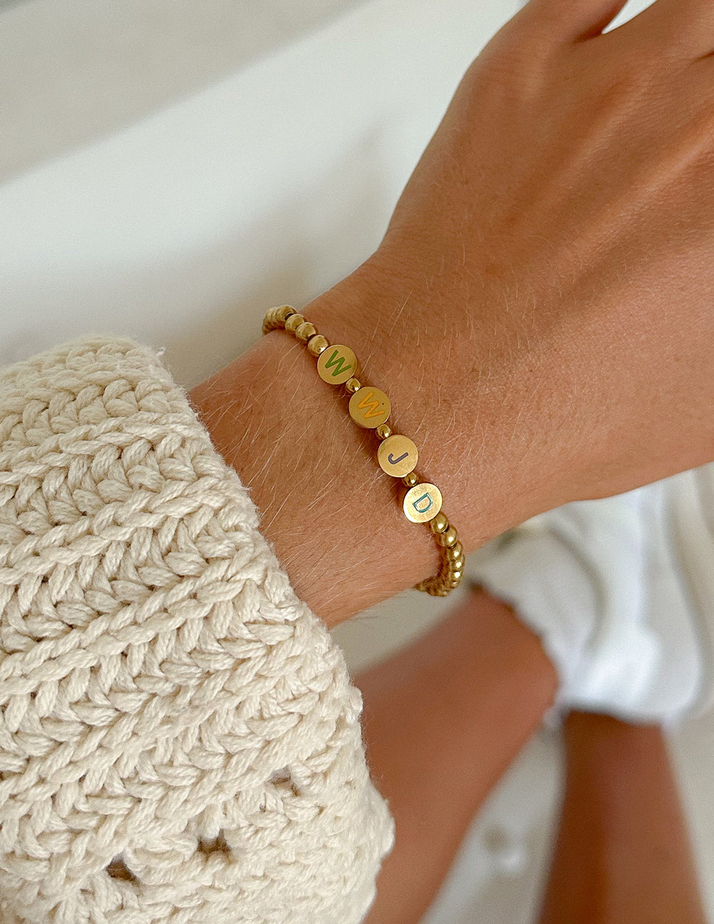 Gold beaded bracelet with colorful letter disks on a wrist