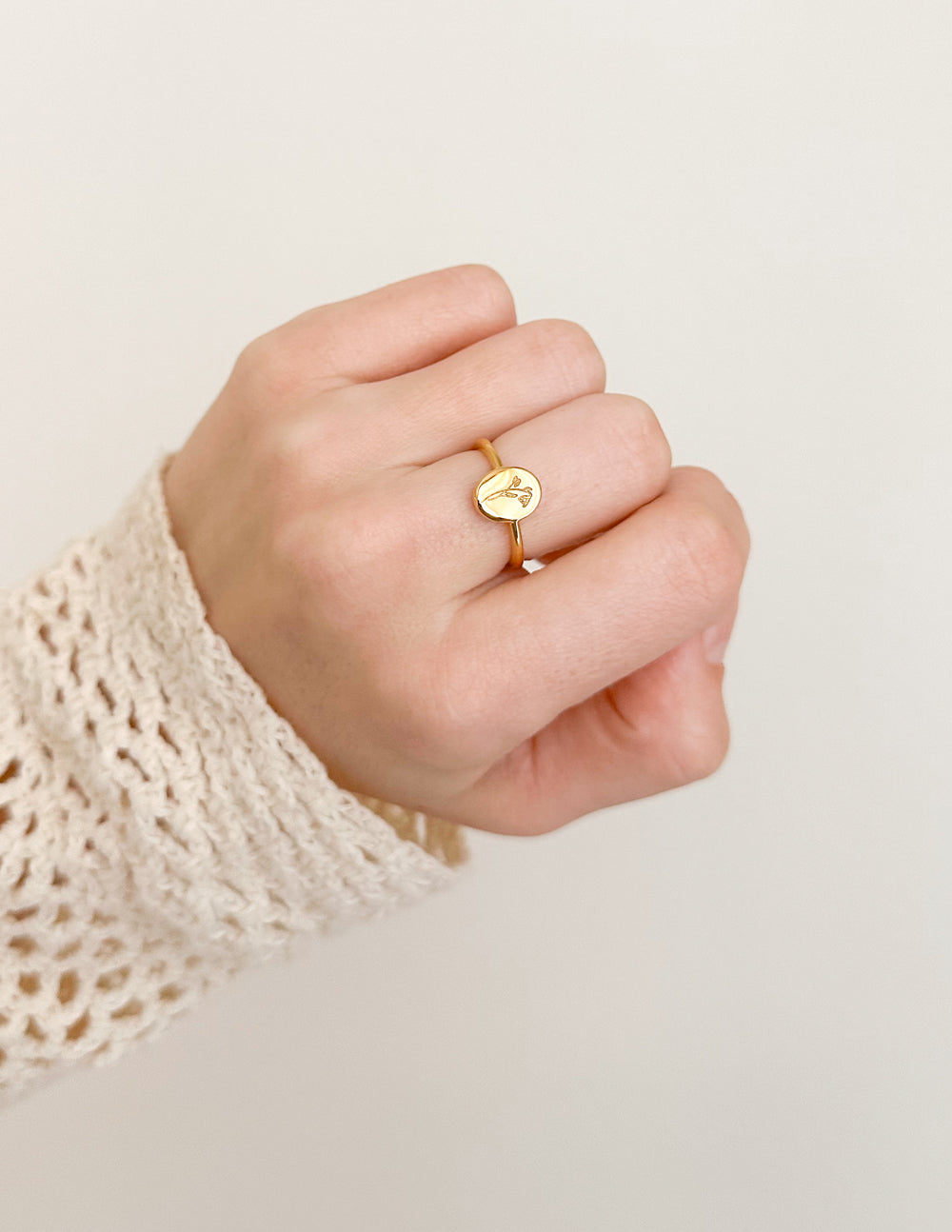 Gold wildflower signet ring with round face and delicate floral engraving on finger