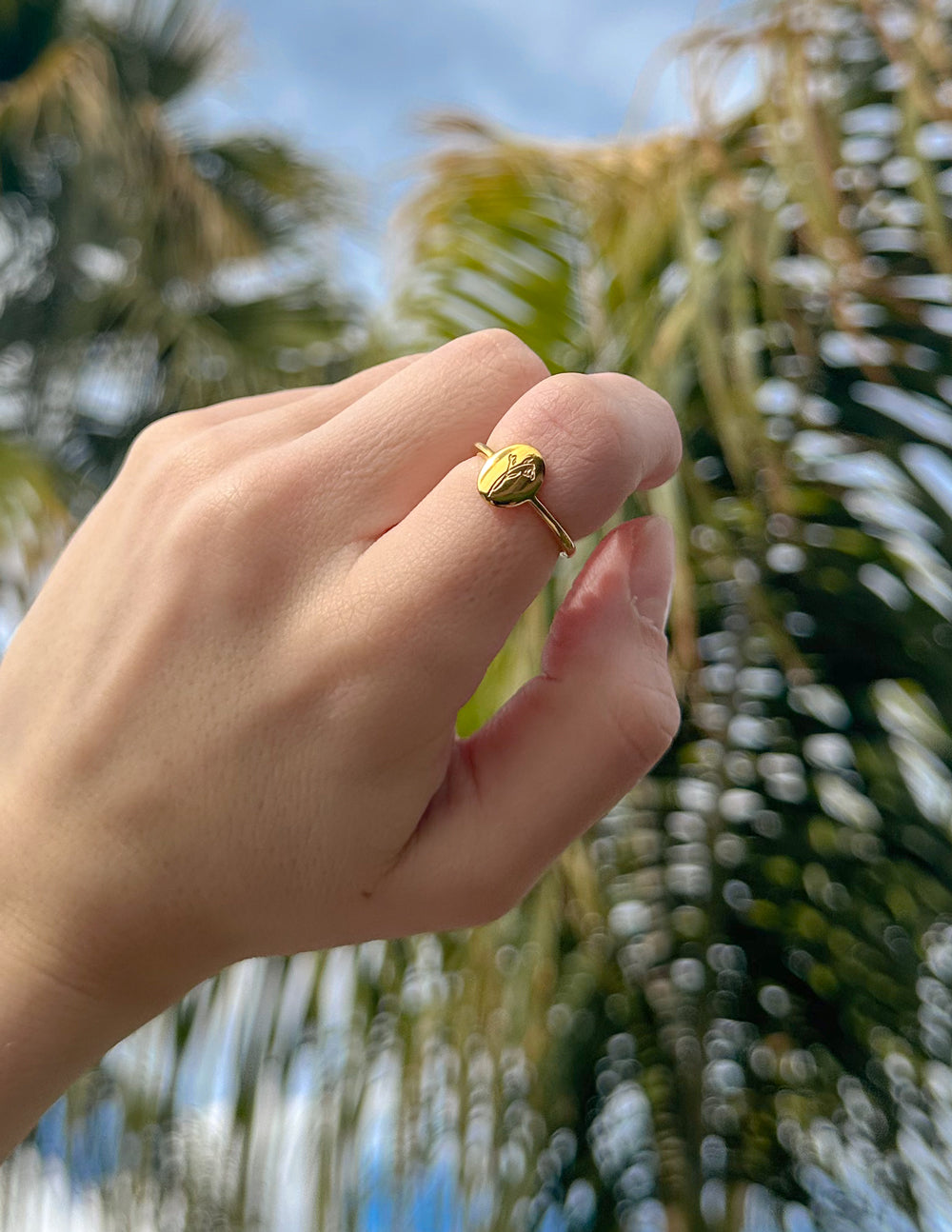 Gold wildflower signet ring on finger, round floral-engraved face and narrow band