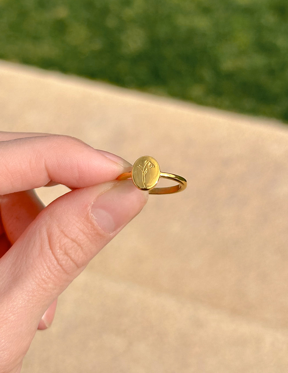 Gold wildflower signet ring close-up: round face with floral engraving and thin band