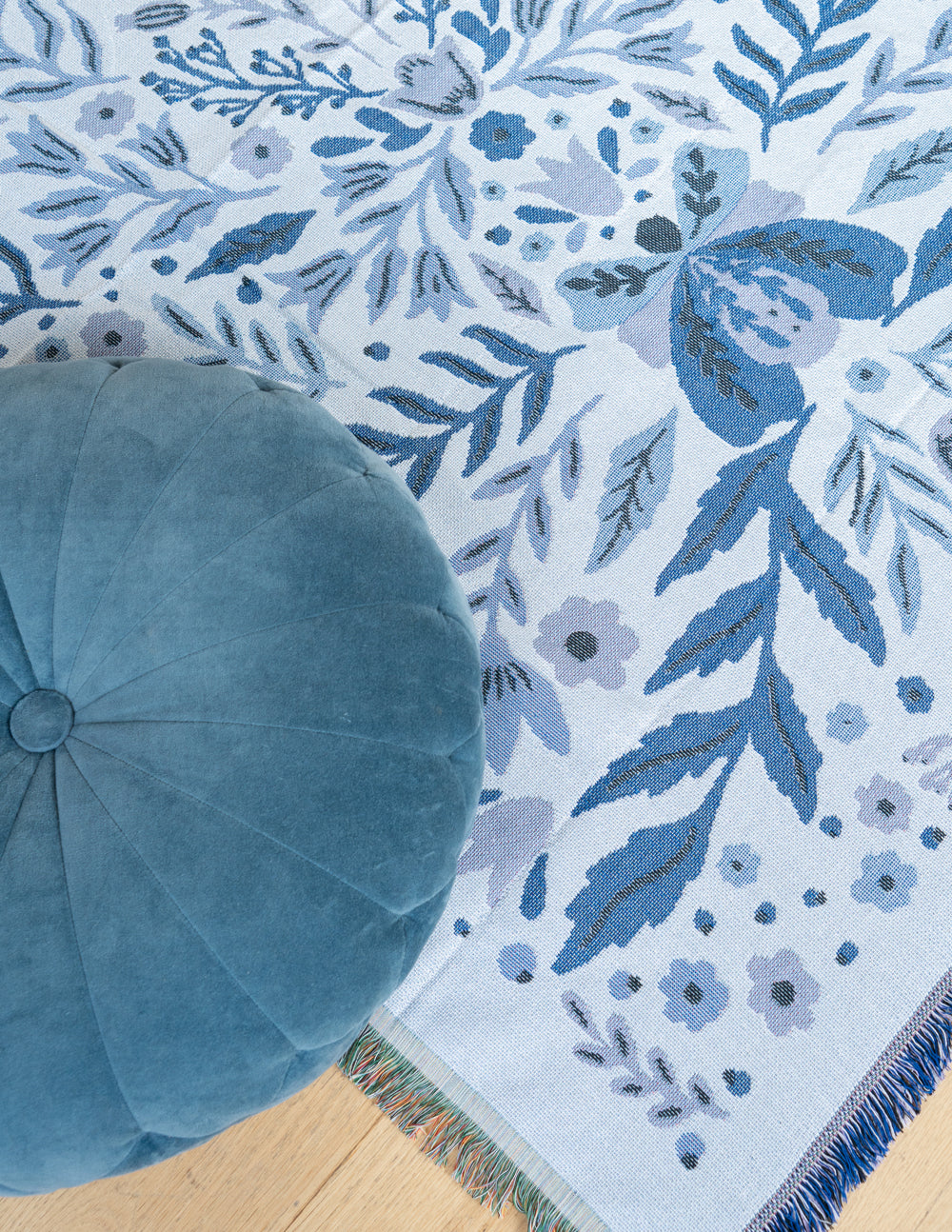 Blue floral throw blanket close-up with fringed border along corner