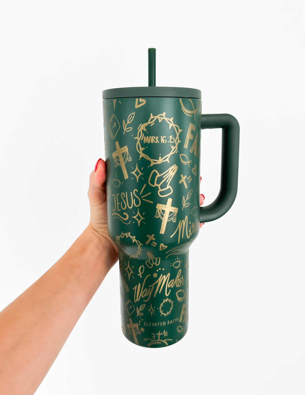 Dark green tumbler with gold faith icons, straw lid and handle, held in hand