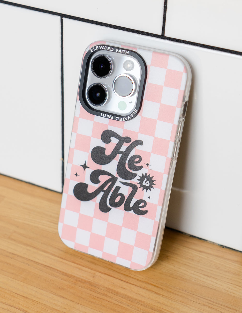 Pink checkered phone case with 'He is Able' lettering and dual camera cutouts