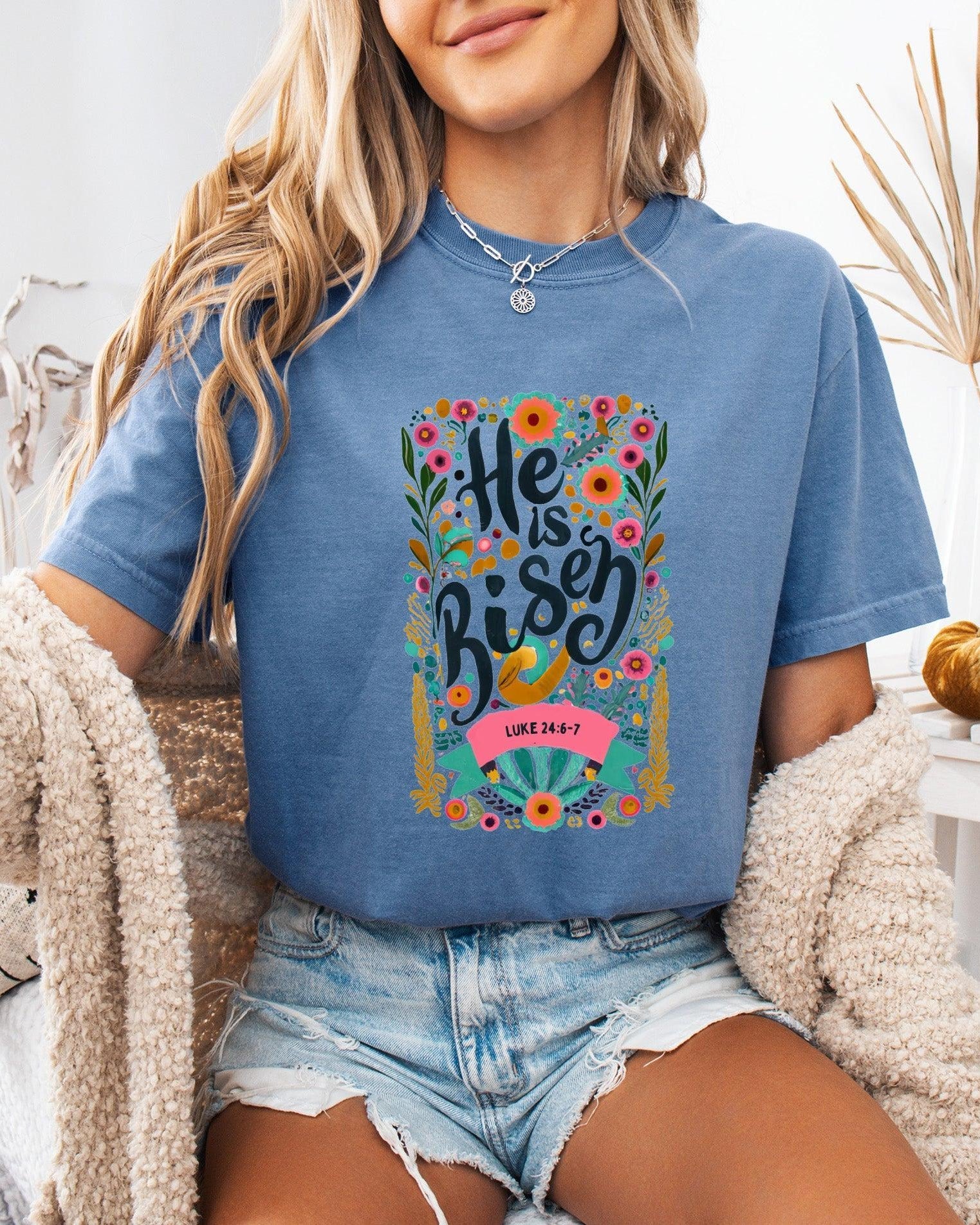 Denim blue crewneck Christian T-shirt with colorful "He is Risen" floral graphic and Luke 24:6-7