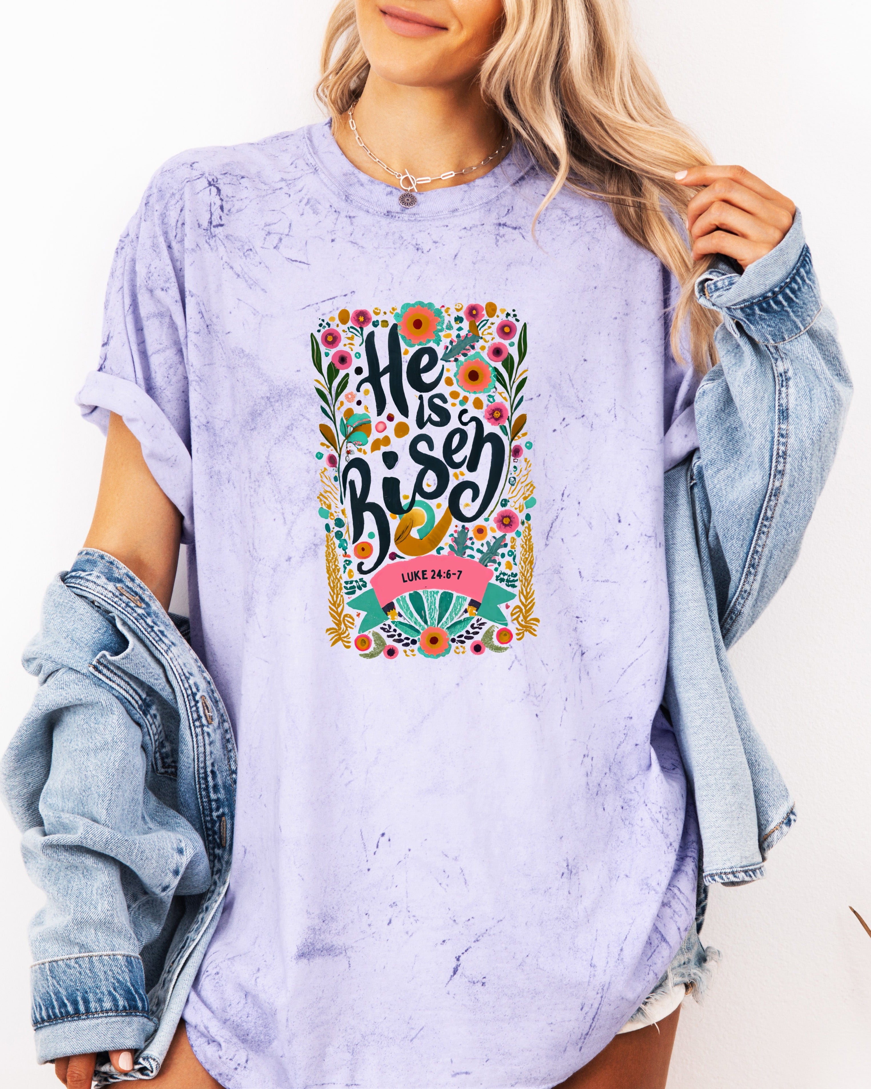 Garment-dyed lavender unisex T-shirt with colorful "He is Risen" front graphic