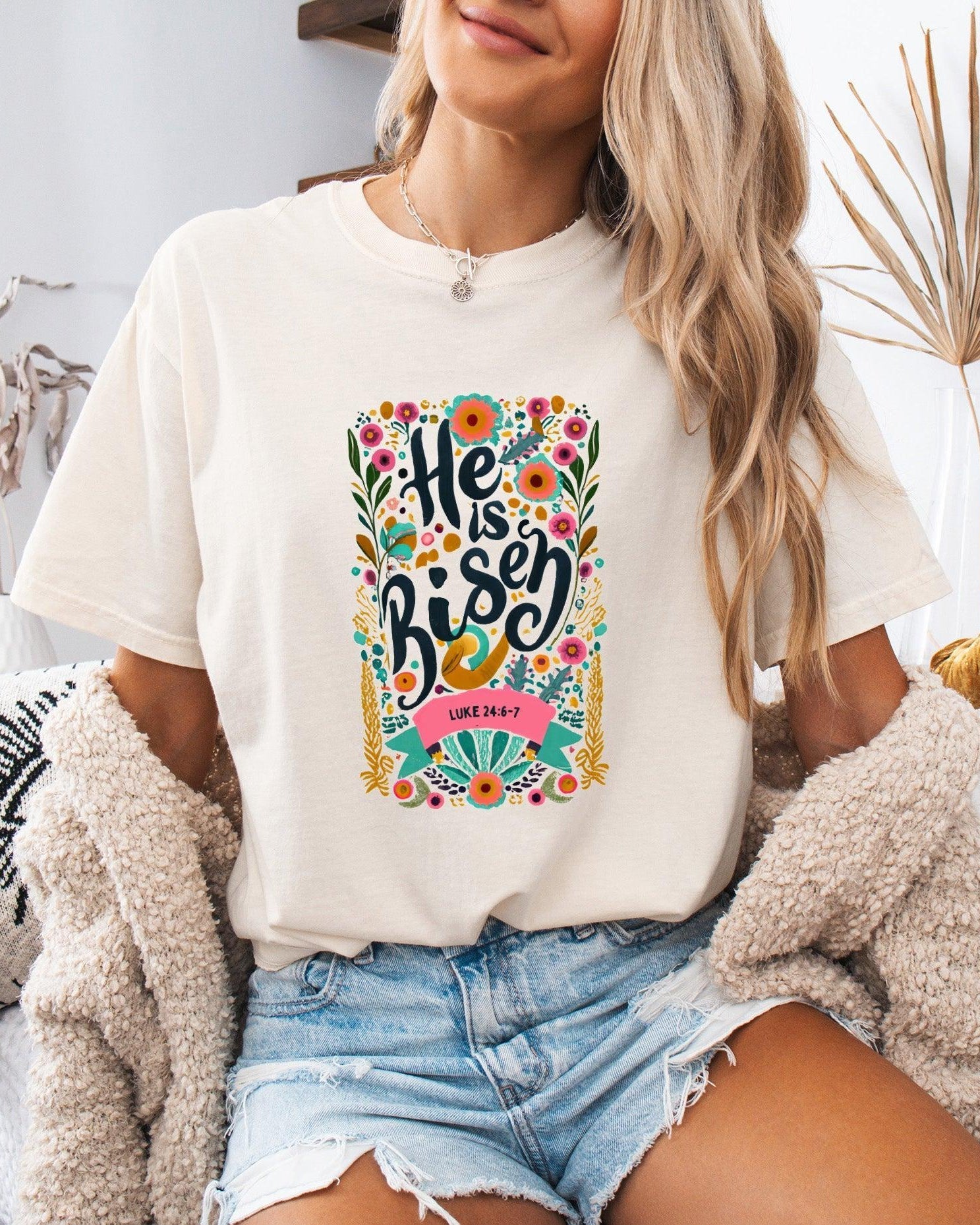 White crewneck Christian T-shirt with colorful "He is Risen" floral graphic and Luke 24:6-7