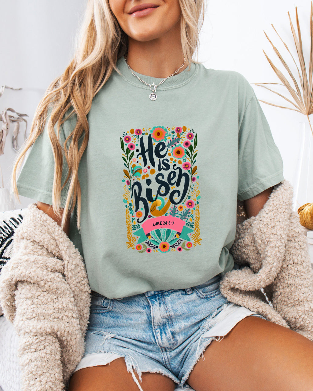 Sage green crewneck Christian T-shirt with colorful "He is Risen" floral graphic and Luke 24:6-7