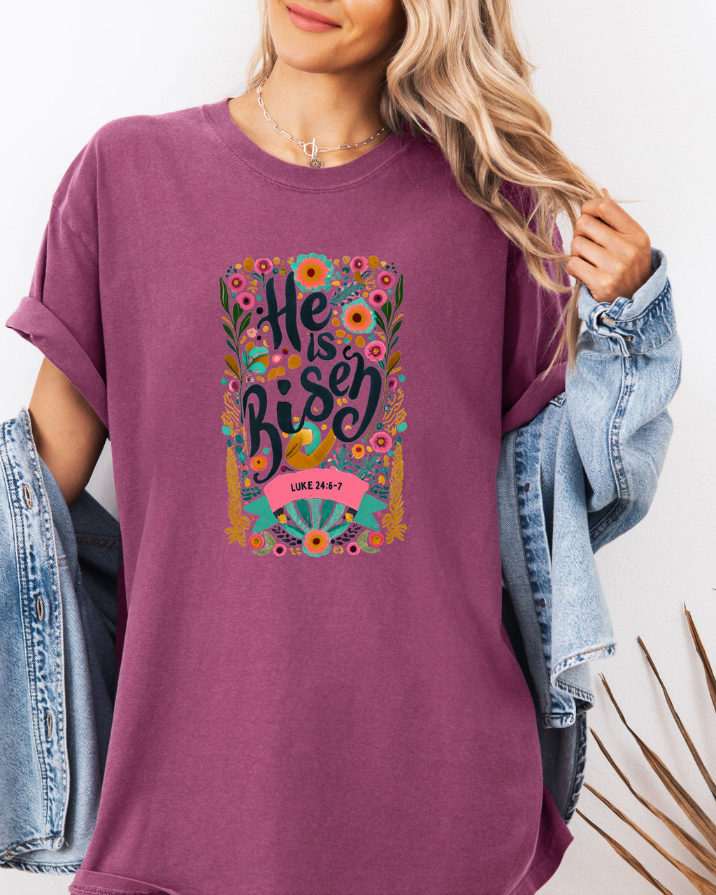 Plum crewneck Christian T-shirt with colorful "He is Risen" floral graphic and Luke 24:6-7