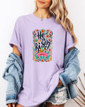 Purple crewneck Christian T-shirt with colorful "He is Risen" floral graphic and Luke 24:6-7