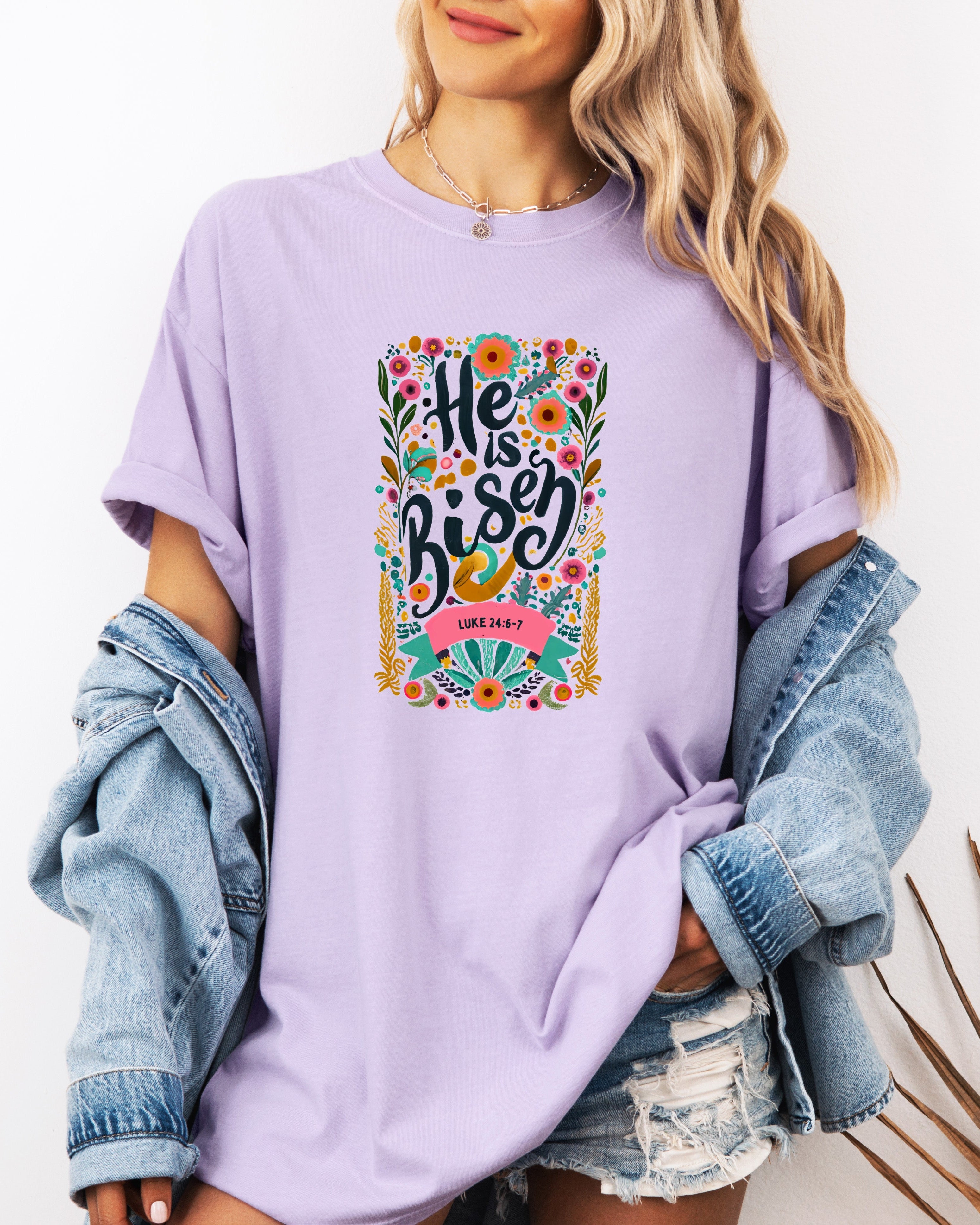 Purple crewneck Christian T-shirt with colorful "He is Risen" floral graphic and Luke 24:6-7