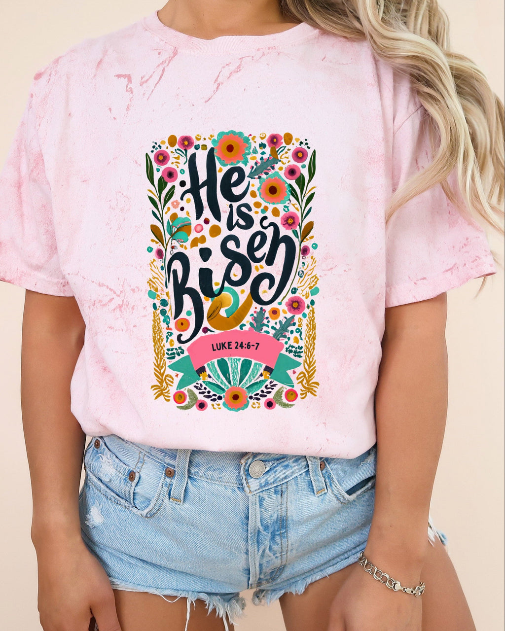 Light pink crewneck Christian T-shirt with colorful "He is Risen" floral graphic and Luke 24:6-7