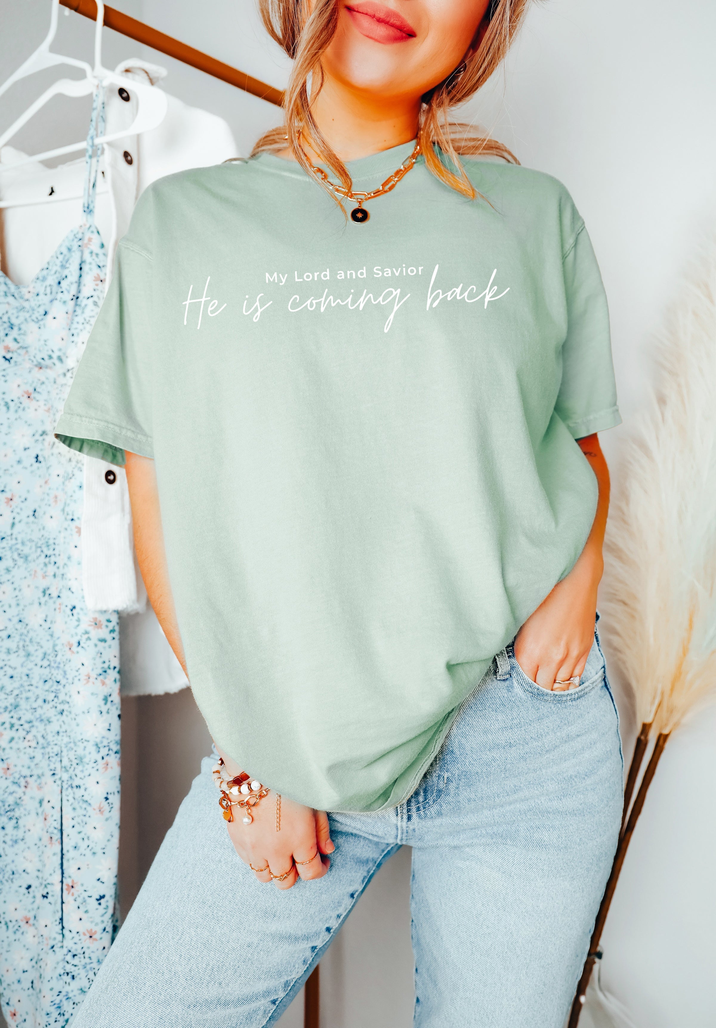Women's sage green graphic T-shirt with “He is coming back” lettering at center