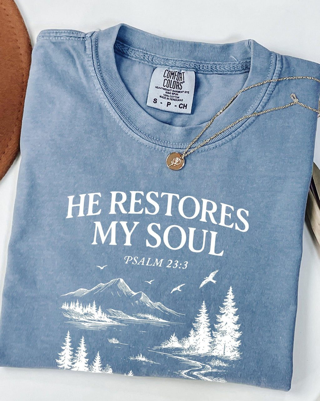 Light blue unisex T-shirt with white “He Restores My Soul” mountain and tree graphic