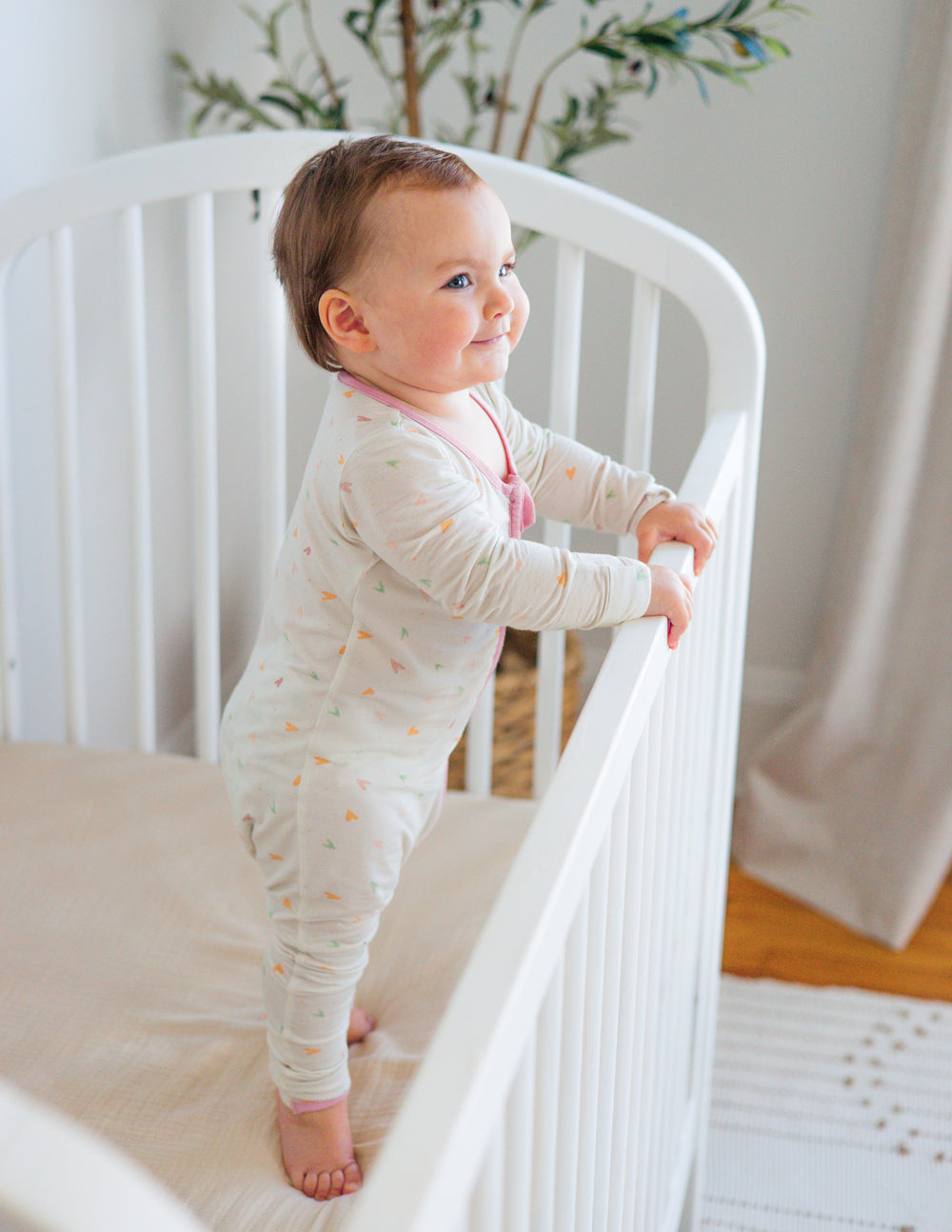 Off-white heart-print footed onesie with pink front zipper and long sleeves.