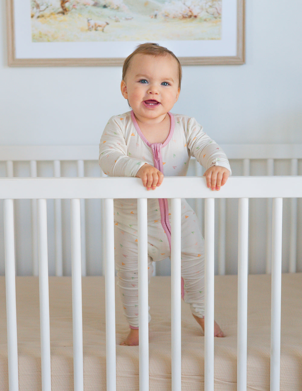 Off-white heart-print footed onesie with pink front zipper, long sleeves.