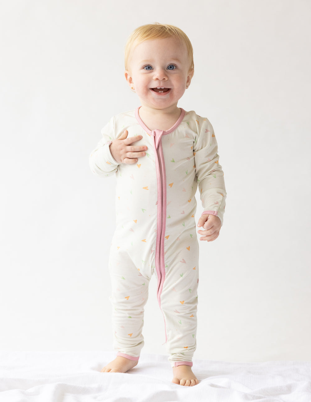 Off-white heart-print footed onesie with pink zipper placket and long sleeves.