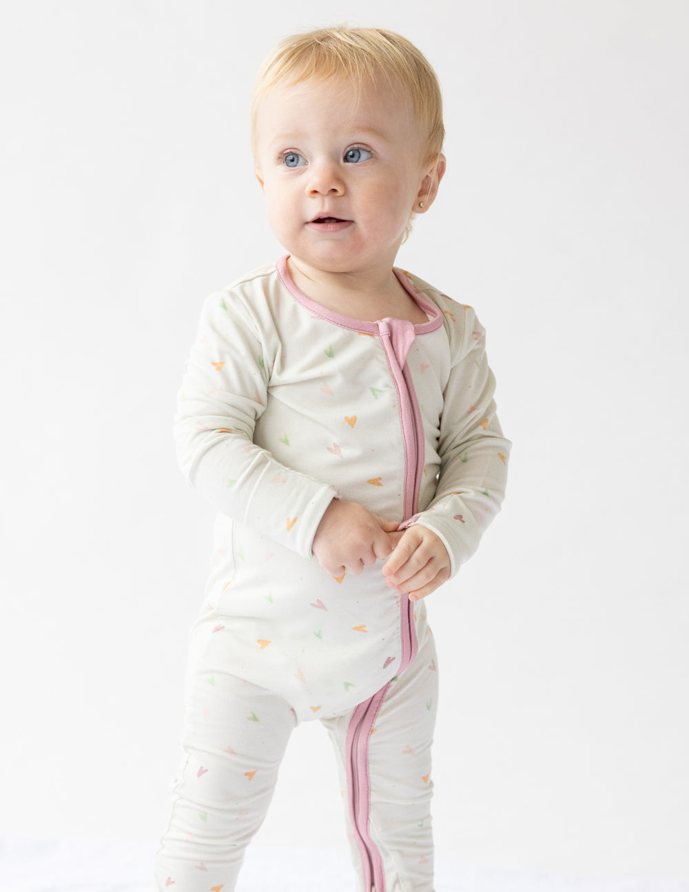 Off-white heart-print footed onesie with pink trim and full-length legs.