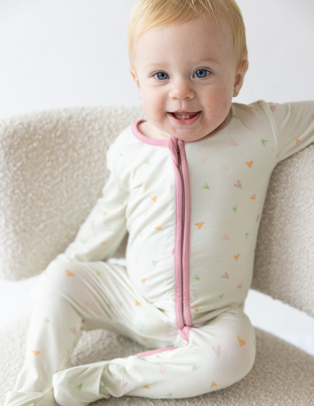 Off-white heart-print footed onesie with pink front zipper and long sleeves.