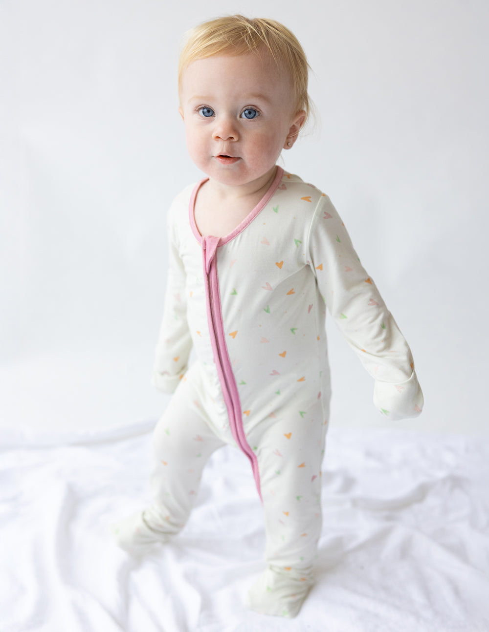 Off-white heart-print footed onesie with pink front zipper, long sleeves.