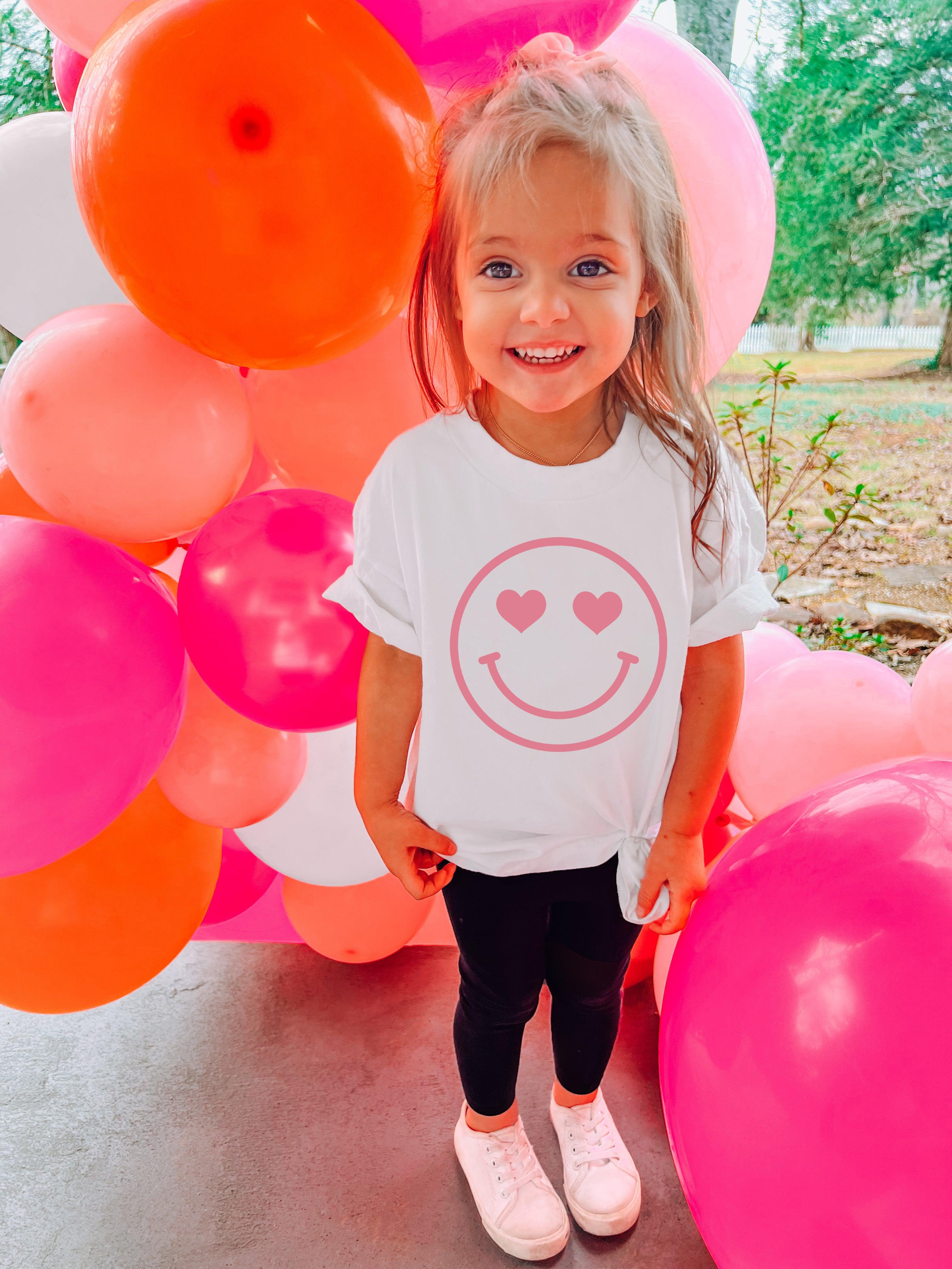White baby girl t-shirt with pink heart-eyed smiley face graphic