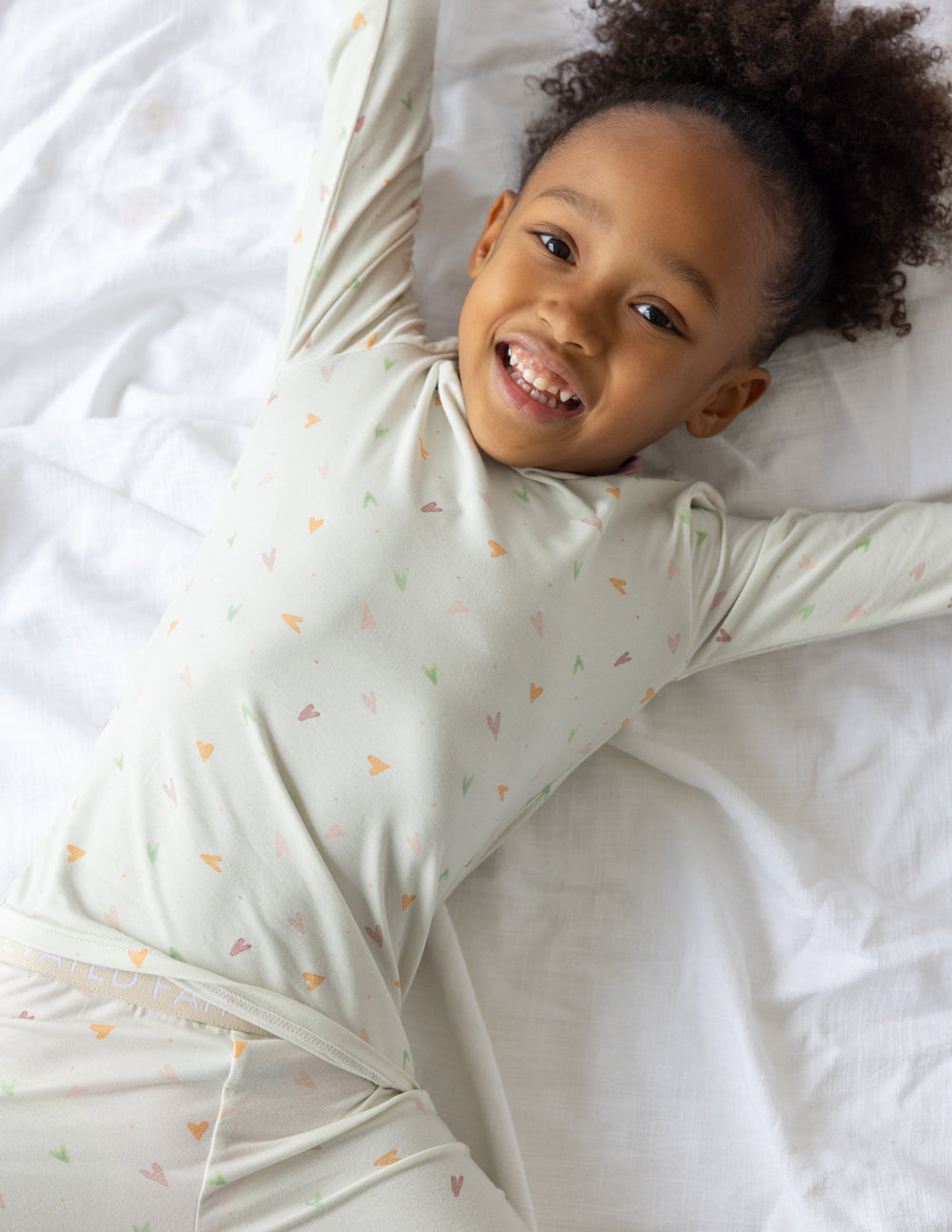 Kids pajama set in light cream with multicolor heart print and pink cuff trim, lying pose