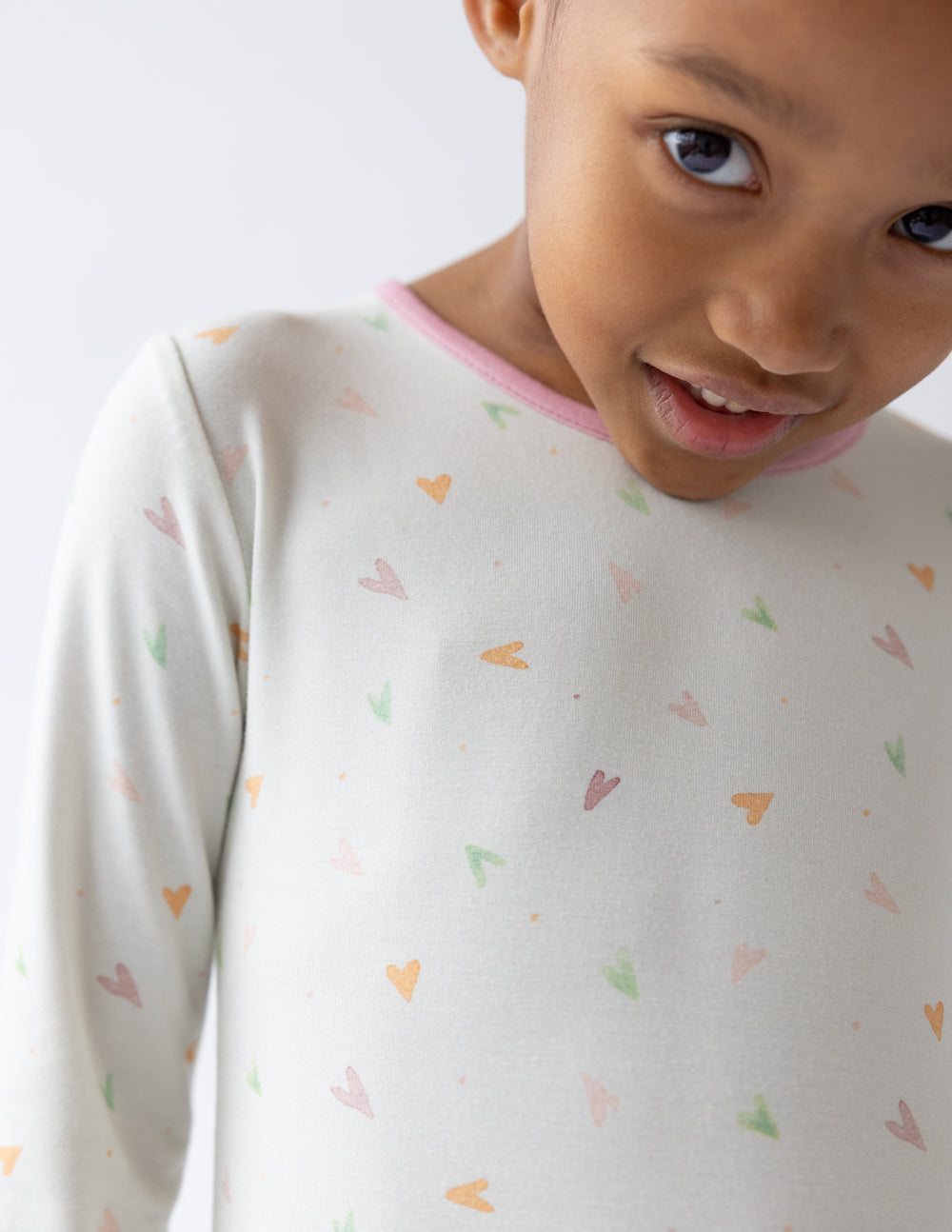 Kids pajama top close-up in light cream knit with multicolor heart print and pink collar trim