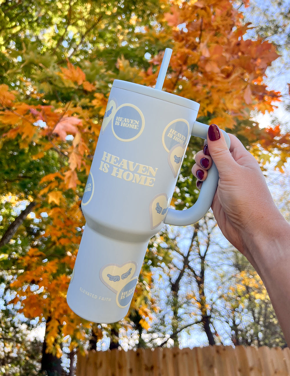 Light blue 40 oz tumbler with straw and handle, held up against autumn trees