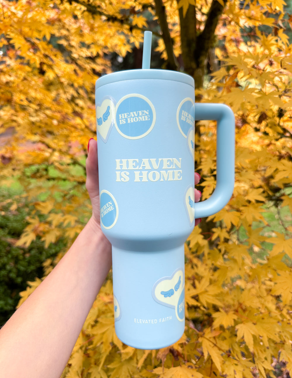 Light blue 40 oz tumbler with straw and handle, held outdoors among autumn leaves