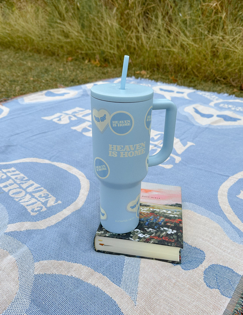 Light blue 40 oz tumbler with straw and handle on a blue patterned blanket outdoors