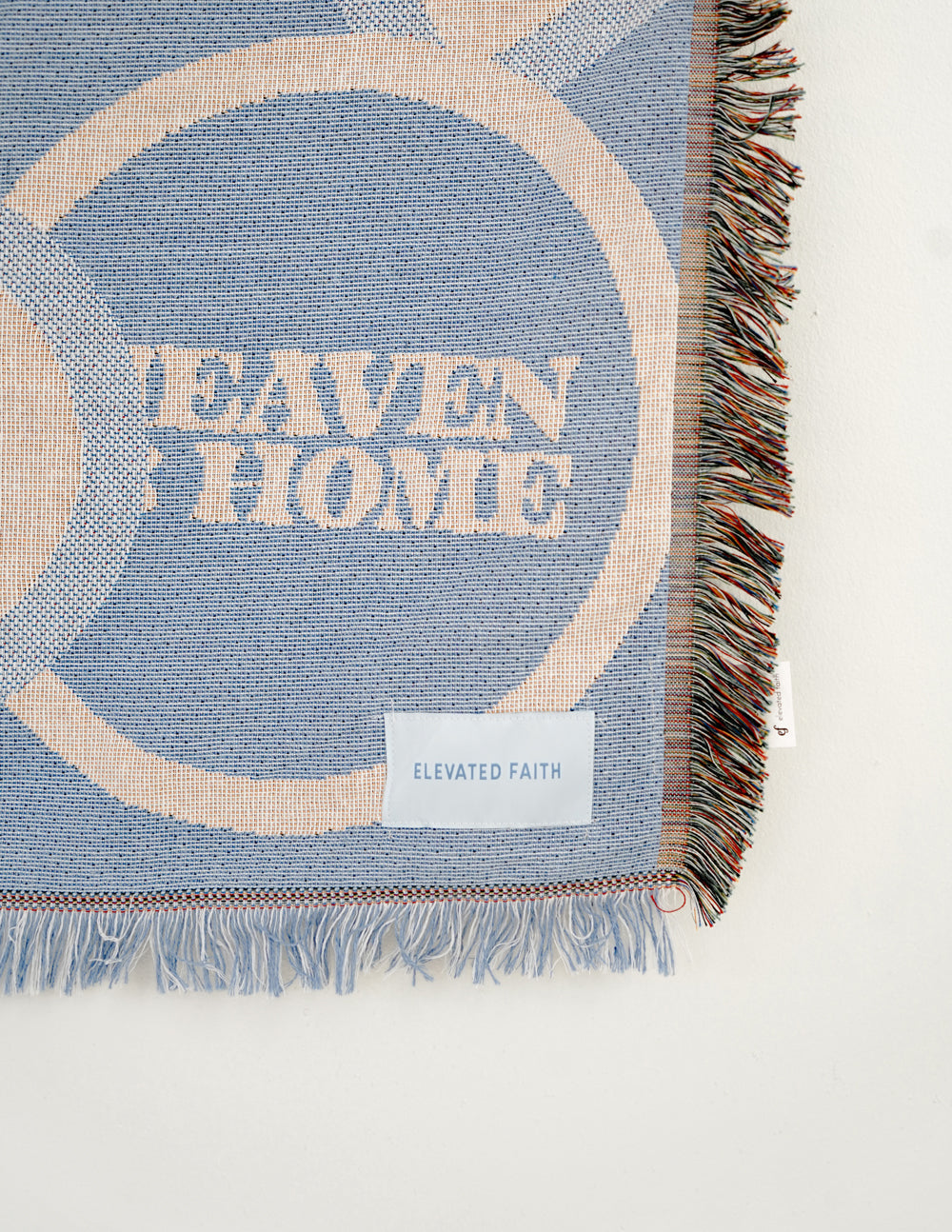 Light blue throw blanket corner with fringes and 'Elevated Faith' fabric label