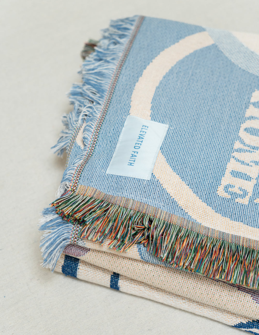 Light blue throw blanket corner with woven label and multicolor fringe trim