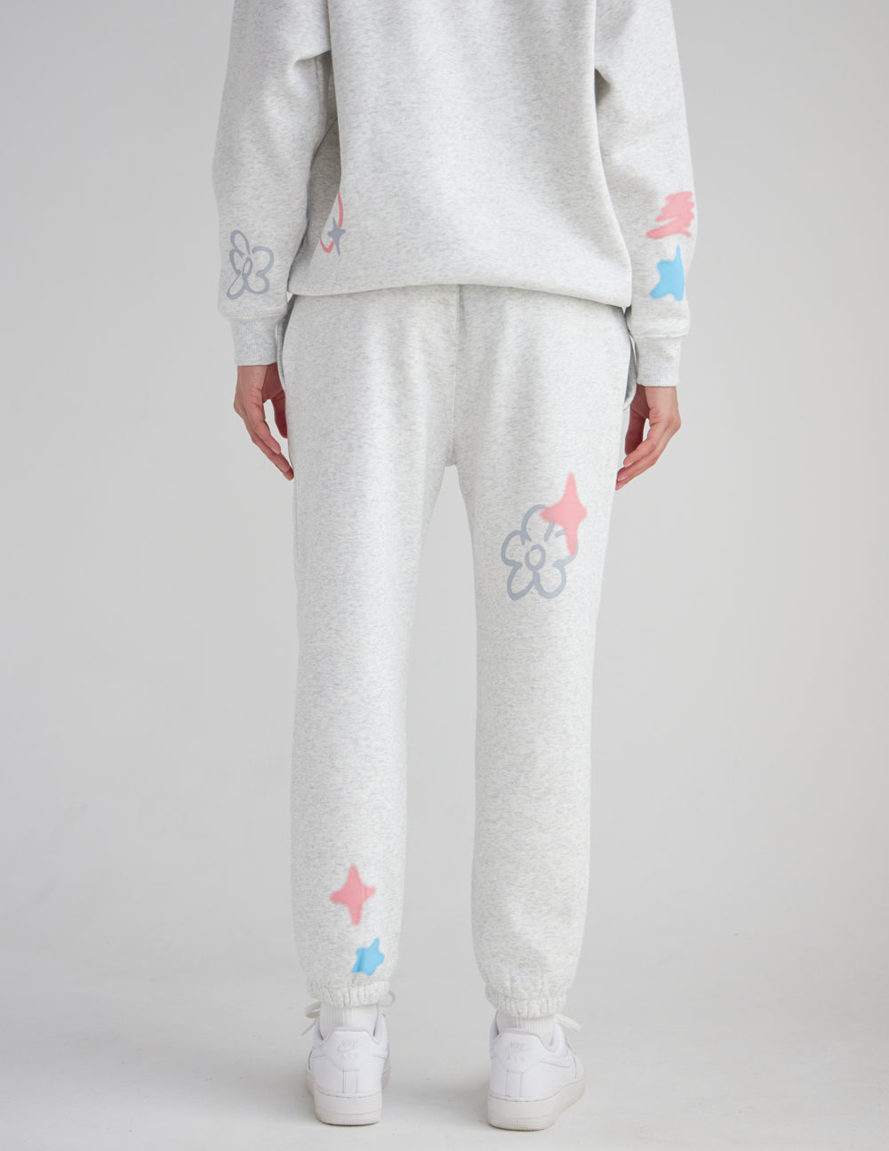 Light gray unisex sweatpants with pastel star, flower, and heart prints on the legs