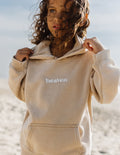 Kids hoodie in light tan with “heaven” logo on the chest and front pocket.