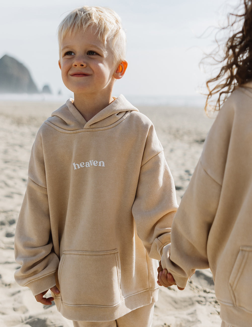 Kids hoodie in light tan with “heaven” logo and hood; front kangaroo pocket.