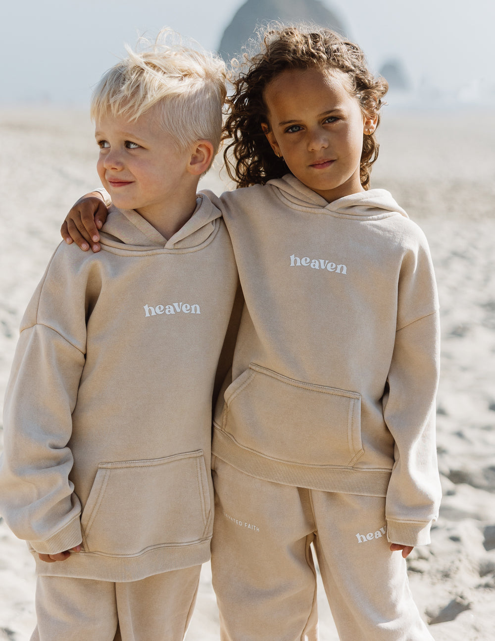 Pair of kids tan hoodies with “heaven” chest logo and front pocket kangaroo.