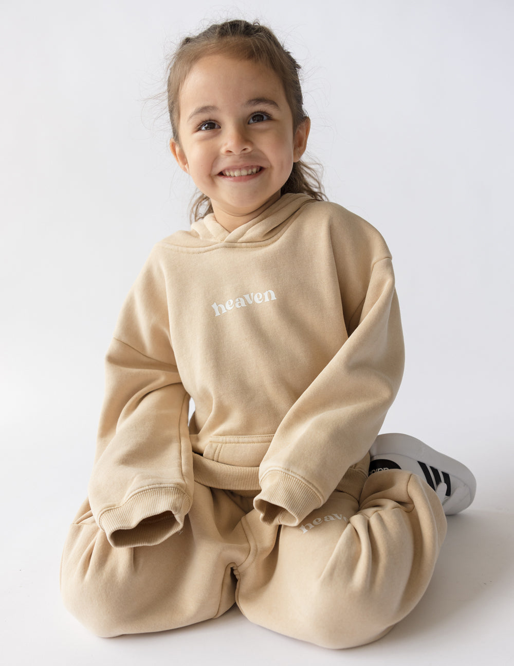 Kids tan hoodie with “heaven” logo, hood, and kangaroo pocket; long sleeves.