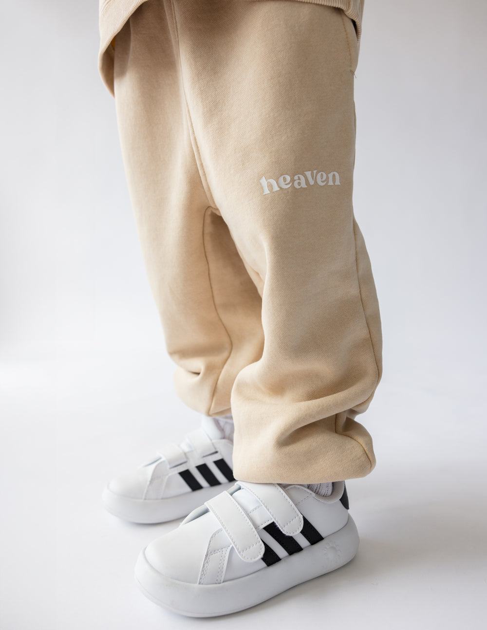 Beige kids sweatpants with elastic cuffs and 'heaven' logo on the leg
