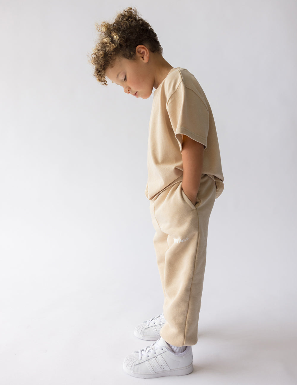 Beige kids sweatpants, side view, with elastic cuffs and 'heaven' logo